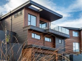 A modern house with wooden and dark panel exterior with glass balcony at Remarkable QT  - Queenstown Holiday Home