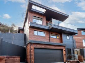 A modern multi-story house with wooden and dark panel exterior and glass balcony at Remarkable QT  Queenstown