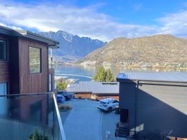 A driveway with cars parked next to modern houses with a lake and mountains in the background at Remarkable QT Queenstown Holiday Home