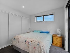 A bedroom with a bed a blanket two pillows a wooden nightstand with a fan a window and a built-in closet with sliding doors at Alex Vineyard - Alexandra Holiday Home in Alexandra