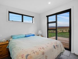A bedroom with a bed two wooden nightstands a fan a window and a sliding glass door leading outside at Alex Vineyard - Alexandra Holiday Home in Alexandra