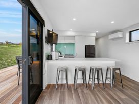 A kitchen area with a counter and four metal stools next to a sliding glass door at Alex Vineyard - Alexandra Holiday Home in Alexandra