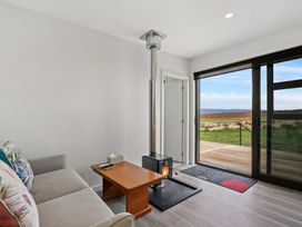 A living room with a sofa and wooden coffee table near a wood stove and sliding glass door at Alex Vineyard - Alexandra Holiday Home in Alexandra