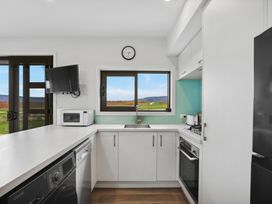 A kitchen with white cabinets countertop appliances dishwasher oven microwave and a window showing outdoor view at Alex Vineyard - Alexandra Holiday Home in Alexandra