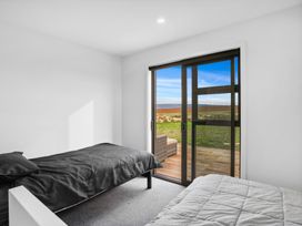 A bedroom with two single beds and a sliding glass door opening to a deck with outdoor furniture at Alex Vineyard - Alexandra Holiday Home in Alexandra