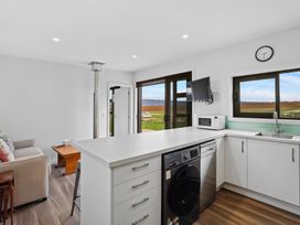 A kitchen with white cabinets and appliances next to a living area with a couch and coffee table at Alex Vineyard - Alexandra Holiday Home in Alexandra