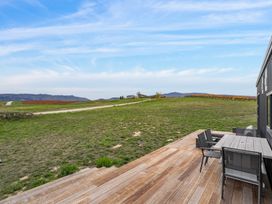 A wooden deck with table and chairs overlooking grassy land and distant hills at Alex Vineyard - Alexandra Holiday Home in Alexandra