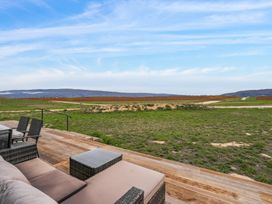 An outdoor wooden deck with patio furniture overlooking a grassy area and fields with mountains in the distance at Alex Vineyard Alexandra Holiday Home