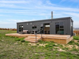 A modern dark gray modular home with wooden deck and outdoor furniture on grass at Alex Vineyard Alexandra Holiday Home Alexandra
