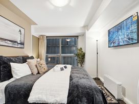 A bedroom with a bed pillows a floor lamp a wall-mounted TV a plant and a window at Cityscape on White - Auckland Central Studio in Auckland Central
