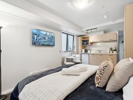 A studio apartment with a bed towels on it a small dining table with two chairs a wall-mounted tv and a kitchenette with cabinets and appliances at Cityscape on White - Auckland Central Studio in Auckland Central