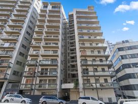 A tall residential building with multiple balconies and parked cars on the street in front of it at Cityscape on White - Auckland Central Studio in Auckland Central