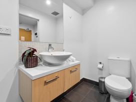 A bathroom with a white sink on a wooden cabinet a mirror a toilet and a trash bin at Cityscape on White - Auckland Central Studio in Auckland Central
