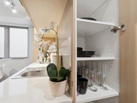 A kitchen with a sink and a white orchid plant on the counter next to an open cabinet with dishes and glasses at Cityscape on White Auckland Central Studio in Auckland Central