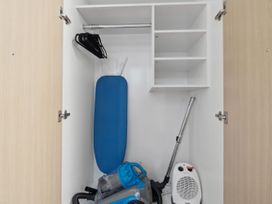 An open white closet with a blue ironing board black hangers a vacuum cleaner and a white space heater at Cityscape on White Auckland Central Studio Auckland Central