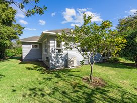 A yard with a fruit tree and a grey house in the background at Bell Cottage - Oakura Holiday Home in Oakura
