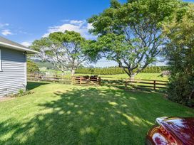 A backyard with green grass trees and a wooden fence next to a gray house at Bell Cottage - Oakura Holiday Home in Oakura