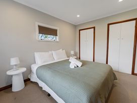 A bedroom with a bed covered with a green blanket two rolled white towels on the bed two white nightstands with lamps and two white closets with wooden frames at Bell Cottage - Oakura Holiday Home in Oakura