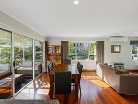 A dining area with a wooden table and black chairs next to a living room with sofas and sliding glass doors at Bell Cottage - Oakura Holiday Home in Oakura
