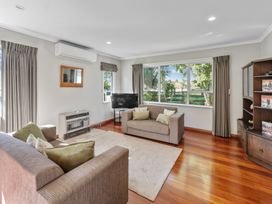 A living room with two sofas a television a wooden cabinet and large windows at Bell Cottage - Oakura Holiday Home in Oakura