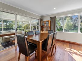 A dining room with a wooden table and six black chairs next to large windows and sliding glass doors at Bell Cottage - Oakura Holiday Home in Oakura