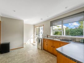 A kitchen with wooden cabinets a stove and a window with blinds overlooking greenery at Bell Cottage - Oakura Holiday Home in Oakura