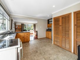 A kitchen with wooden cabinets a stove and a sink overlooking a living area with large windows at Bell Cottage - Oakura Holiday Home in Oakura