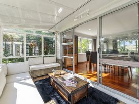 A sunroom with wicker sofas and a wooden coffee table next to a dining room with a wooden table and chairs at Bell Cottage - Oakura Holiday Home in Oakura