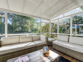 A sunroom with wicker sofas and a wooden coffee table surrounded by large windows at Bell Cottage - Oakura Holiday Home in Oakura