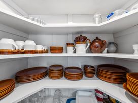 A kitchen cabinet with brown and white ceramic dishes cups and pots at Bell Cottage - Oakura Holiday Home in Oakura