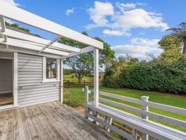 A wooden deck with white railing and pergola overlooking a grassy yard with trees at Bell Cottage - Oakura Holiday Home in Oakura