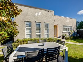 An outdoor dining area with a table and six chairs in a garden next to a house with textured walls and multiple windows at Coastal Charm - Napier Holiday Home in Napier