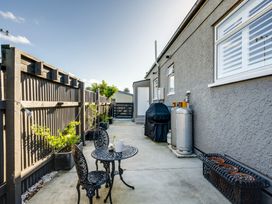 A narrow outdoor patio with a small black metal table and chairs along a fenced area with potted plants and a barbecue grill at Coastal Charm - Napier Holiday Home in Napier