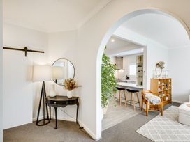 A corner with a black table lamp and round mirror next to an archway opening to a kitchen with bar stools at Coastal Charm in Napier