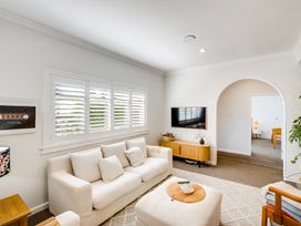 A living room with a beige sofa white shutters a wall-mounted TV and an ottoman at Coastal Charm Napier Holiday Home in Napier
