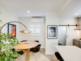 A dining area with a round wooden table and black chairs next to a kitchen with white countertops and a sliding door at Coastal Charm  Napier Holiday Home in Napier