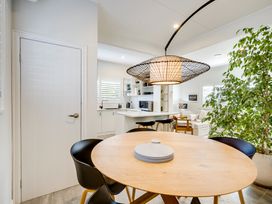 A dining area with a round wooden table and black chairs next to a kitchen with white cabinets and a large plant at Coastal Charm  Napier Holiday Home in Napier