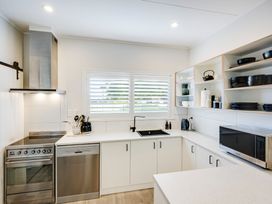 A kitchen with stove dishwasher sink microwave and open shelves with dishes at Coastal Charm - Napier Holiday Home in Napier