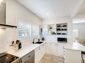 A kitchen with white cabinets black sink and open shelves with dishes at Coastal Charm - Napier Holiday Home in Napier