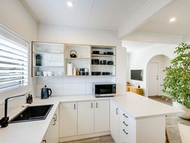 A kitchen with white cabinets black sink microwave and open shelves with dishes at Coastal Charm - Napier Holiday Home in Napier