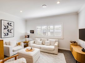 A living room with a sofa armchair ottoman wooden sideboard and window shutters at Coastal Charm - Napier Holiday Home in Napier
