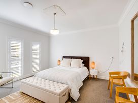 A bedroom with a bed nightstands lamps a bench a chair and windows with shutters at Coastal Charm Napier Holiday Home in Napier