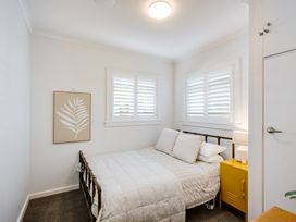 A bedroom with a bed two windows a yellow nightstand and a framed leaf print on the wall at Coastal Charm Napier Holiday Home in Napier