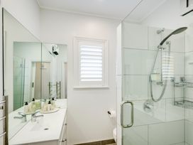 A bathroom with a sink and mirror on the left and a glass-enclosed shower on the right at Coastal Charm - Napier Holiday Home in Napier