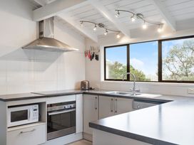 A kitchen with a stove oven microwave toaster sink and window showing trees at Waiake Family Retreat - Auckland Holiday Home in Auckland