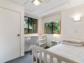 A bedroom with a bed desk chair nightstand and two windows at Waiake Family Retreat Auckland Holiday Home in Auckland