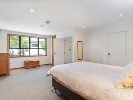 A bedroom with a bed a wooden chest a dresser windows and two doors at Waiake Family Retreat - Auckland Holiday Home in Auckland