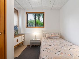 A small bedroom with a single bed next to a white nightstand with a lamp and a wooden cabinet under a window at Waiake Family Retreat Auckland Holiday Home