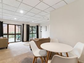 A dining area with a round white table and four white chairs next to a living room with brown sofas and large windows at Waiake Family Retreat Auckland Holiday Home in Auckland