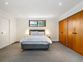 A bedroom with a bed and two bedside lamps between two wooden closets at Waiake Family Retreat in Auckland